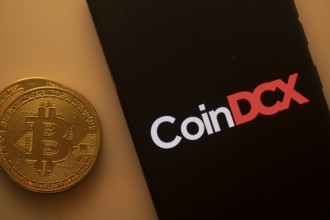 Bitcoin coin beside a black phone screen displaying the CoinDCX logo