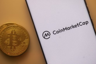 Bitcoin coin beside a white phone screen displaying the CoinMarketCap logo