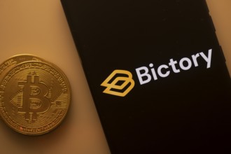 Bitcoin coin beside a black phone screen displaying the Bictory logo