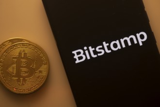 Bitcoin coin beside a black phone screen displaying the Bitstamp logo