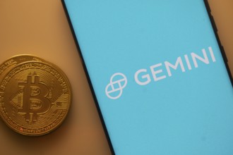 Gemini logo on a smartphone screen alongside a Bitcoin coin