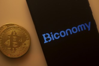 Bitcoin coin beside a black phone screen displaying the Biconomy logo
