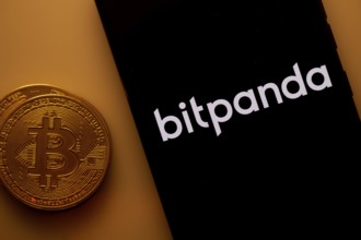 Bitpanda logo on a smartphone screen beside a Bitcoin coin