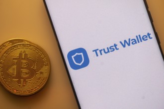 Trust Wallet logo on a smartphone near a Bitcoin coin