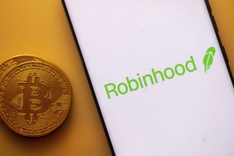 Robinhood logo displayed on a smartphone next to a Bitcoin coin