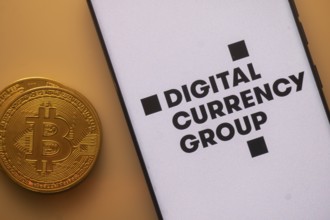 Bitcoin coin next to a smartphone with Digital Currency Group logo on white background