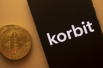 Bitcoin coin adjacent to a phone displaying Korbit logo on a black background