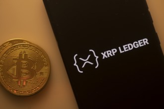 Bitcoin coin next to a phone displaying XRP Ledger logo on a black background