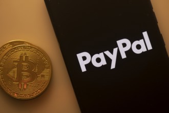 PayPal logo on smartphone screen next to Bitcoin, highlighting digital payments and financial