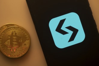 Unidentified logo on smartphone beside Bitcoin, emphasizing cryptocurrency and blockchain