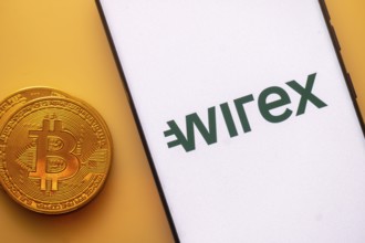 Bitcoin coin next to a phone displaying Wirex logo on white screen