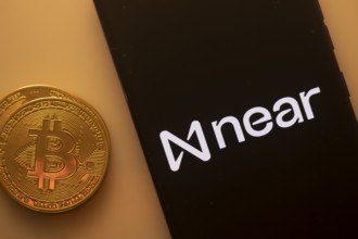 Bitcoin coin beside a phone displaying Near Protocol logo on black screen