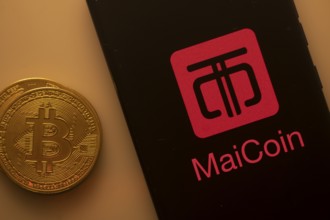Bitcoin coin beside phone with MaiCoin logo on black background