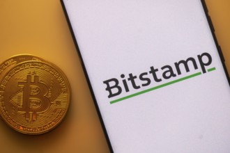 Bitcoin coin next to phone showing Bitstamp logo on white background