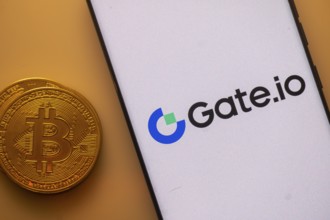 Gate.io logo on a smartphone screen next to a Bitcoin standing on an orange backdrop