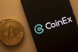 CoinEx logo displayed on a smartphone screen near a Bitcoin coin on an orange background