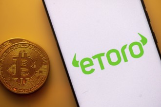Etoro logo on a smartphone screen next to a Bitcoin coin on an orange background