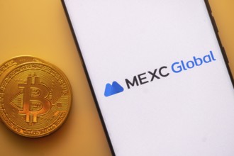 MEXC Global logo on smartphone screen beside a Bitcoin, emphasizing cryptocurrency and technology