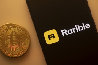 Bitcoin coin beside a phone showing Rarible logo on black screen