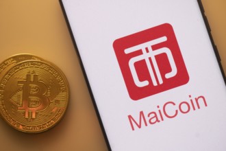 Bitcoin coin beside a phone displaying MaiCoin logo on white screen