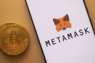 Bitcoin coin alongside a phone showing MetaMask logo on white screen