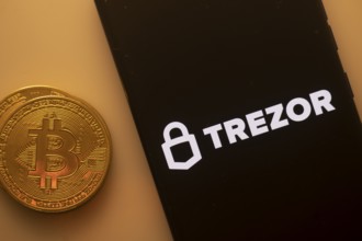 Bitcoin coin beside a phone with Trezor logo on a black screen