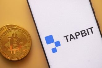 Bitcoin coin beside a phone displaying Tapbit logo on white screen