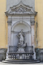 Baroque statue of a saint in a niche on a church wall, surrounded by decorative stone architecture,