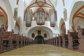 Interior of a church with detailed wooden benches and an impressive organ on the ceiling, St
