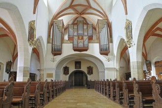 View into the interior of a church with high vaulted ceilings and an impressive organ on the wall,