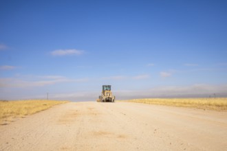 In the remote desert near Solitaire, Namibia, a tractor levels a dirt road across golden sand dunes