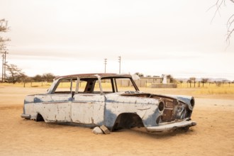 Solitaire's car graveyard in Namibia features rusted vintage cars near small desert buildings, set