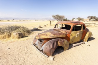 Solitaire's car graveyard in Namibia features rusted vintage cars near small desert buildings, set