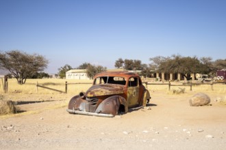 Solitaire's car graveyard in Namibia features rusted vintage cars near small desert buildings, set