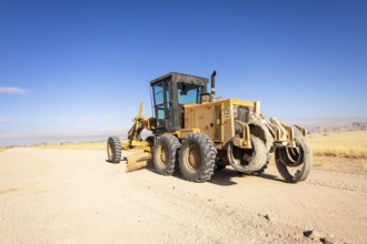In the remote desert near Solitaire, Namibia, a tractor levels a dirt road across golden sand dunes