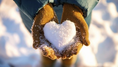 Hands wearing yellow gloves holding a heart made of snow during a cold winter day, AI generated