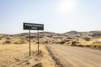A road sign marks Spreetshoogte Pass in Namibia, with a gravel road winding through golden