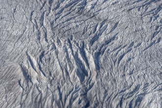 Crevasses and streaks mark the surface of the glacier. The sunlight highlights these unique