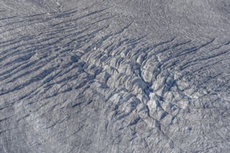 Crevasses and streaks mark the surface of the glacier. The sunlight highlights these unique