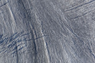 Crevasses and streaks mark the surface of the glacier. The sunlight highlights these unique