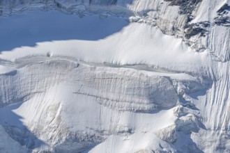 A large blanket of snow covers the rocks in the mountains. The sky is clear and reflects the serene