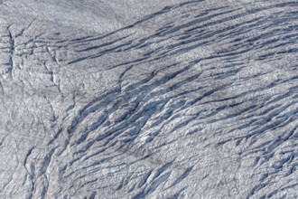 Crevices mark the surface of the glacier. The landscape is illuminated by daylight, highlighting