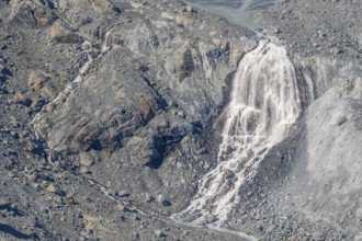 Waterfalls flow over a glacier surrounded by rocks and debris. This natural phenomenon is caused by