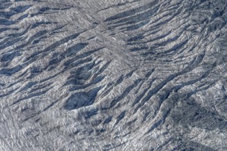 Crevices mark the surface of the glacier. The landscape is illuminated by daylight, highlighting