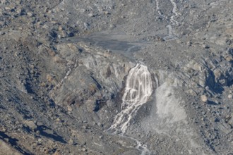 Waterfalls flow over a glacier surrounded by rocks and debris. This natural phenomenon is caused by
