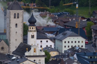 Firefighters standing on a roof fighting a fire in a house in the town centre of San Candido, San
