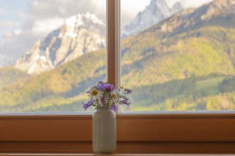 A vase with meadow flowers stands on the windowsill in the background the mountains of the