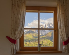 View through a window to the Dolomites in the foreground a small vase with meadow flowers on the