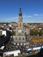Imposing clock tower with lively market activity and market stalls in the foreground, under blue