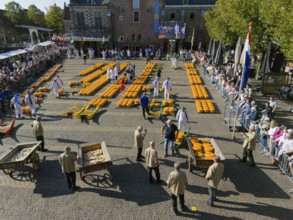 Traditional market with cheese wagon and participants, crowds and historic building in the